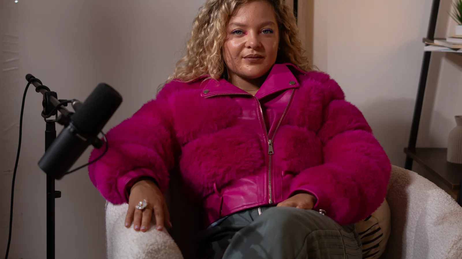 Invitée assise dans un fauteuil avec un micro sur pied, cadre large de studio à Genève