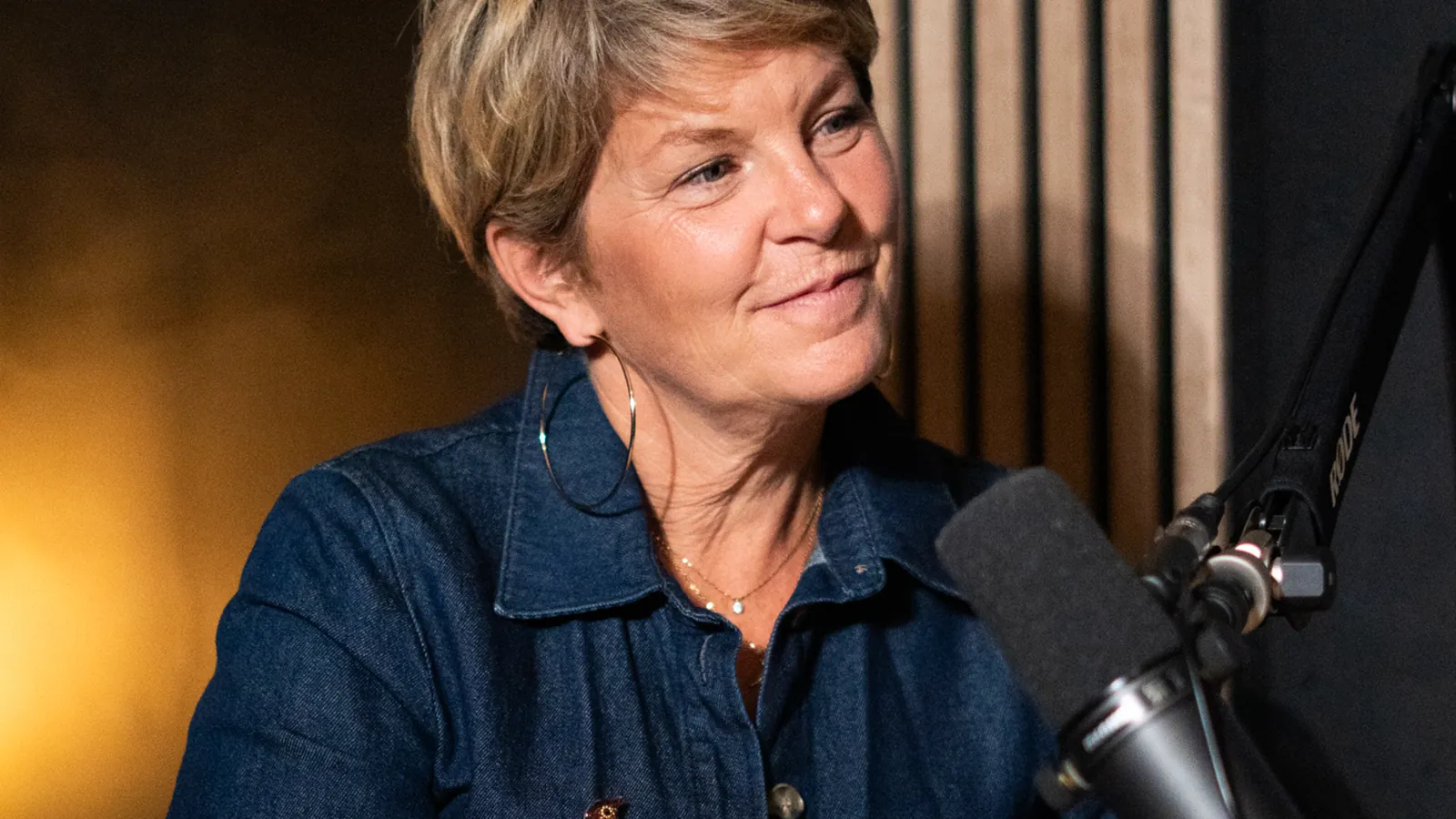 Femme aux cheveux courts en chemise en jean au micro dans un studio podcast