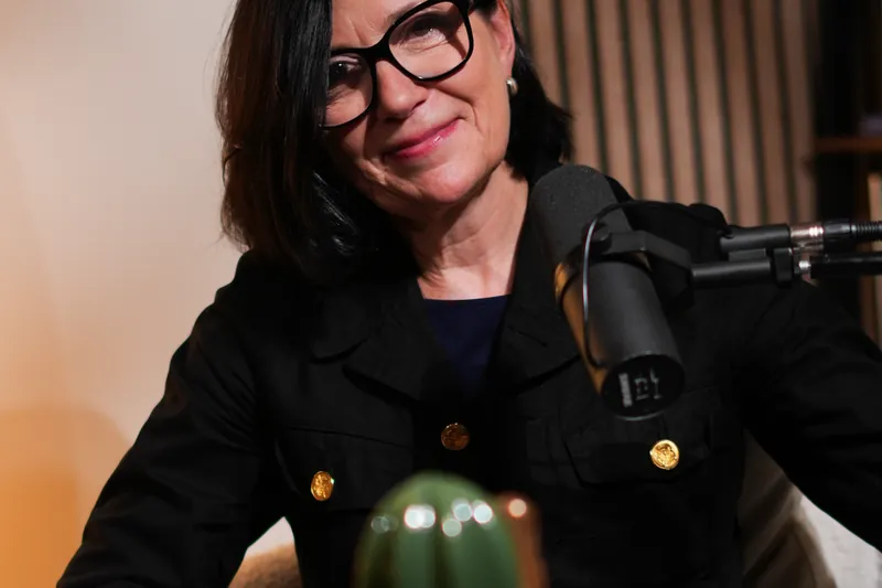 Femme à lunettes en veste noire au micro dans un studio podcast