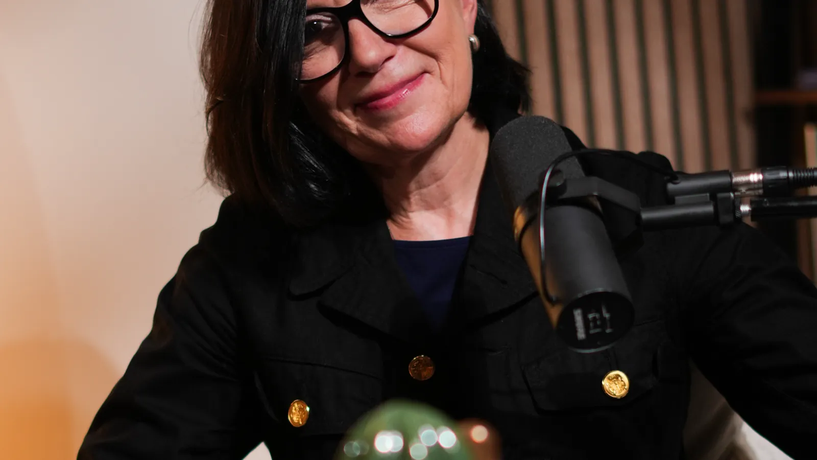 Femme à lunettes en veste noire au micro dans un studio podcast