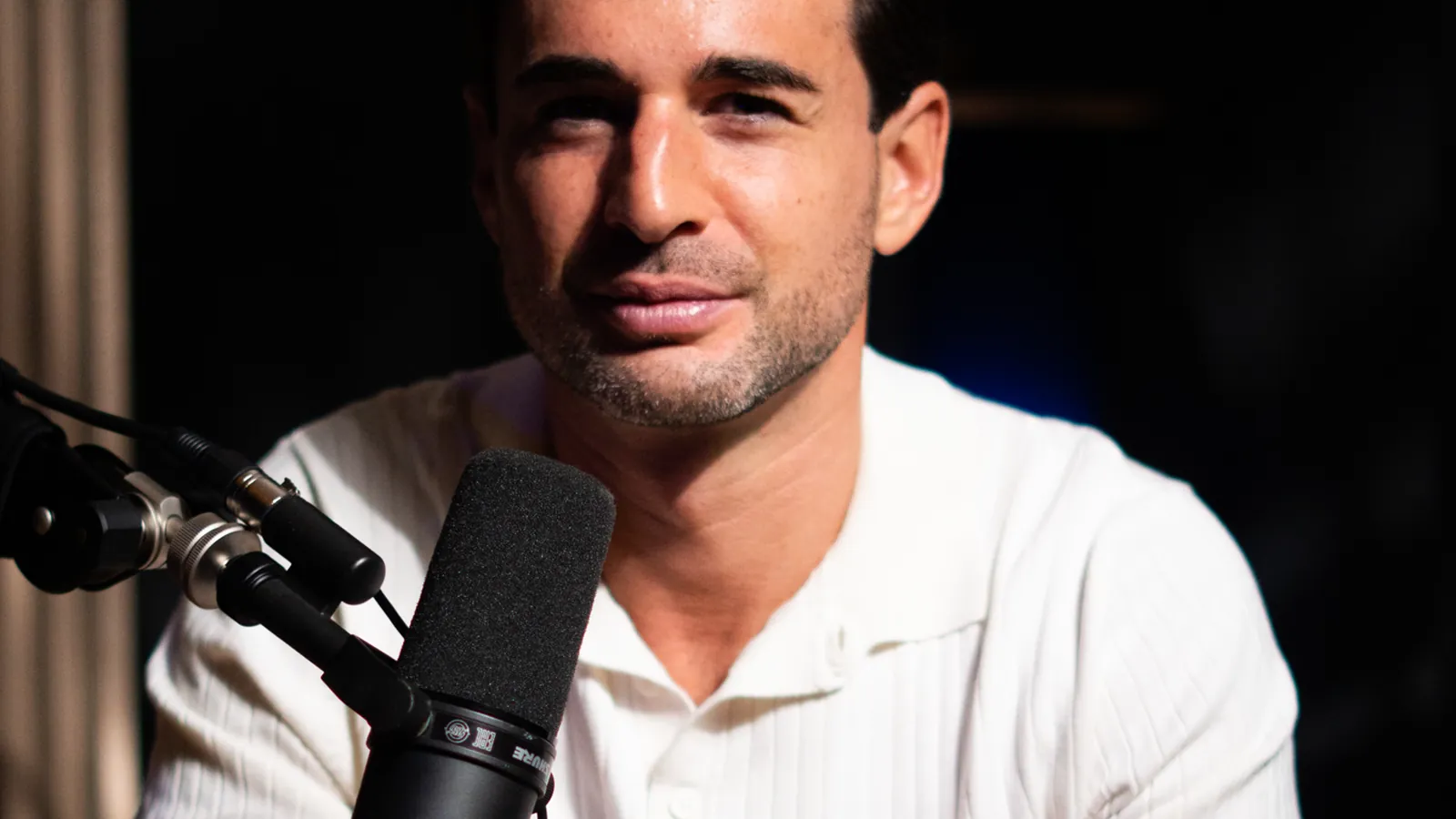 Homme en polo blanc au micro, éclairage sombre de studio