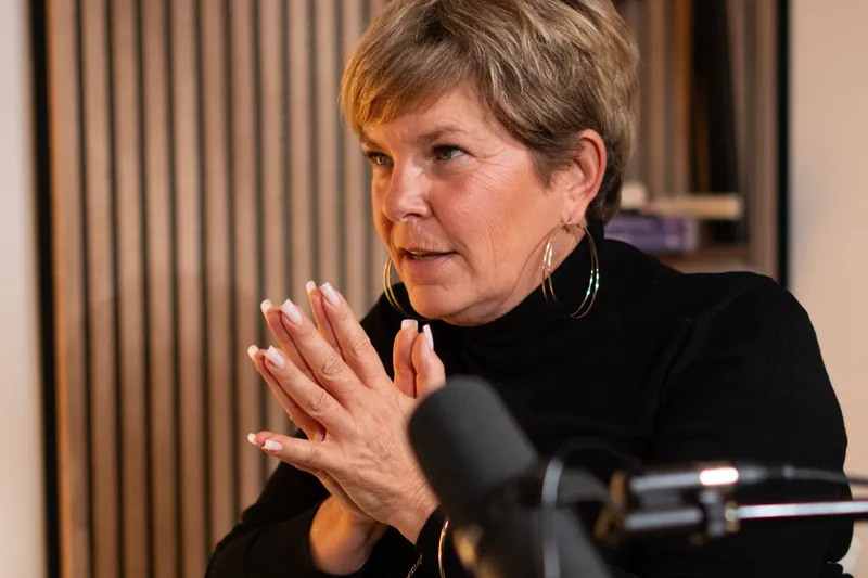 Femme aux cheveux courts parlant au micro, les mains jointes, dans un studio