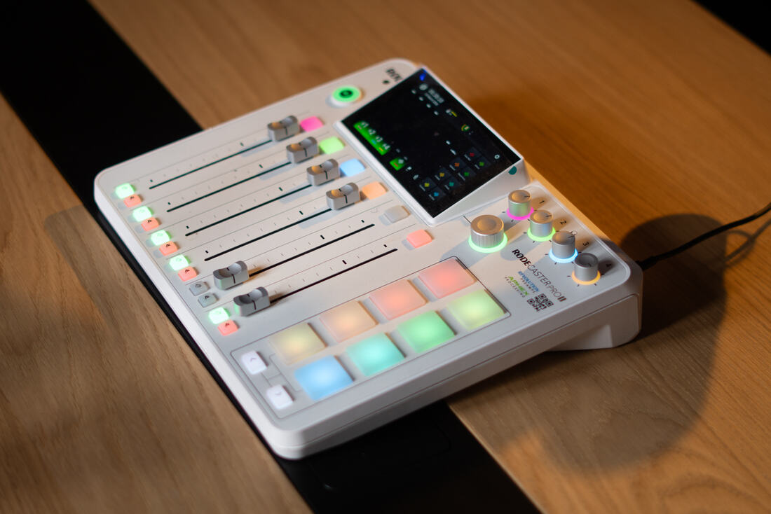 White RØDECaster console on the studio's wooden table, coloured pads lit up