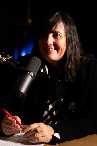 Smiling guest at the mic, pen in hand, blue light behind her